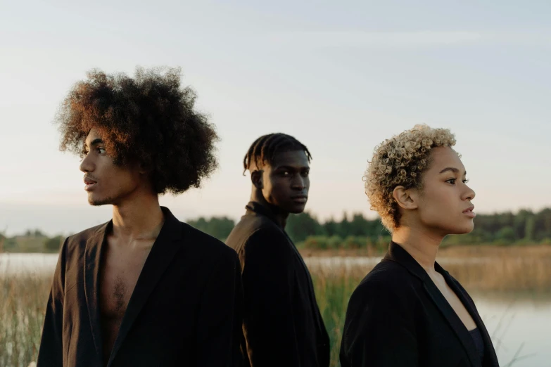 three people standing next to each other near a body of water, an album cover, by Carey Morris, pexels contest winner, afrofuturism, natural hair, nordic folk, perfect faces, wearing black modern clothes