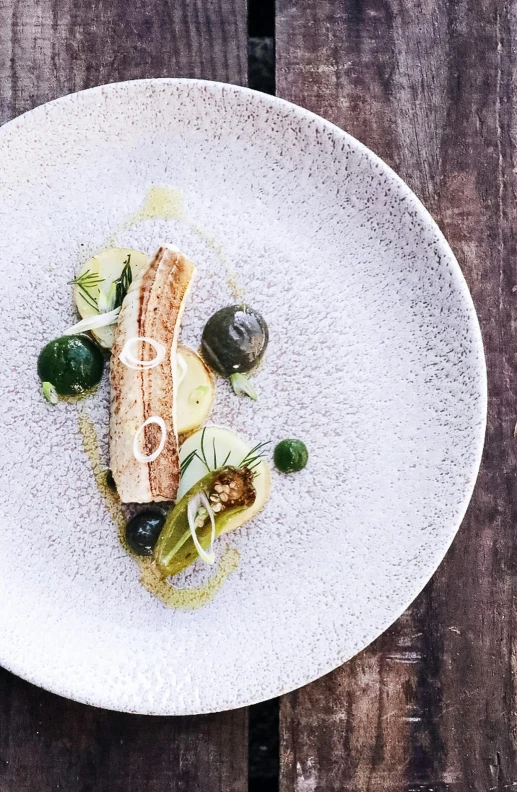 a white plate topped with food on top of a wooden table, inspired by Barthélemy Menn, unsplash, fish skin, olive, peter guthrie, dwell