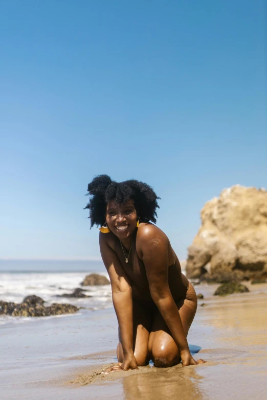 a woman kneeling on top of a sandy beach, by Jessie Algie, unsplash, renaissance, afro hair, malibu canyon, is wearing a swimsuit, a still of a happy