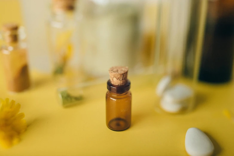 a close up of a bottle of essential oil on a table, by Emma Andijewska, unsplash, on yellow paper, miniatures, brown resin, glass jar
