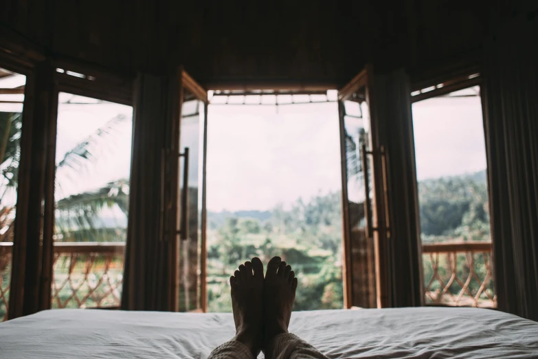 a person laying on a bed in front of a window, pexels contest winner, happy toes, lush vista, wood cabin in distance, detailed legs towering over you