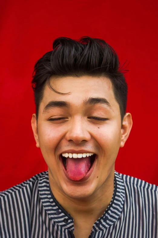 a man sticking his tongue out in front of a red background, inspired by John Luke, sumatraism, lgbtq, official photo, asian features, grinning lasciviously