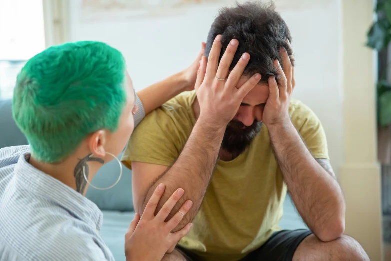 a man sitting on top of a couch next to a woman, trending on pexels, short unkempt green hair, devastated, multicoloured, in pain