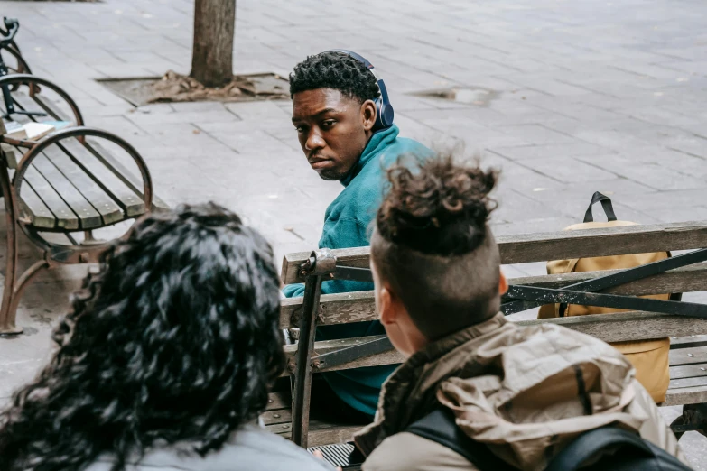 a group of people sitting on top of a wooden bench, trending on unsplash, realism, black teenage boy, curls on top of his head, on the streets, looking backwards