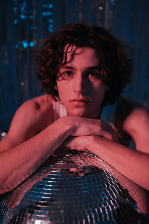 a man laying on top of a disco ball, an album cover, by Nathalie Rattner, trending on pexels, portrait of timothee chalamet, looking serious, curls, bisexual lighting