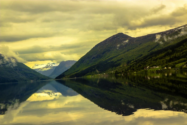 a body of water surrounded by mountains under a cloudy sky, a picture, by Julia Pishtar, norway fjord, golden hour photo, reflections. shady, conde nast traveler photo