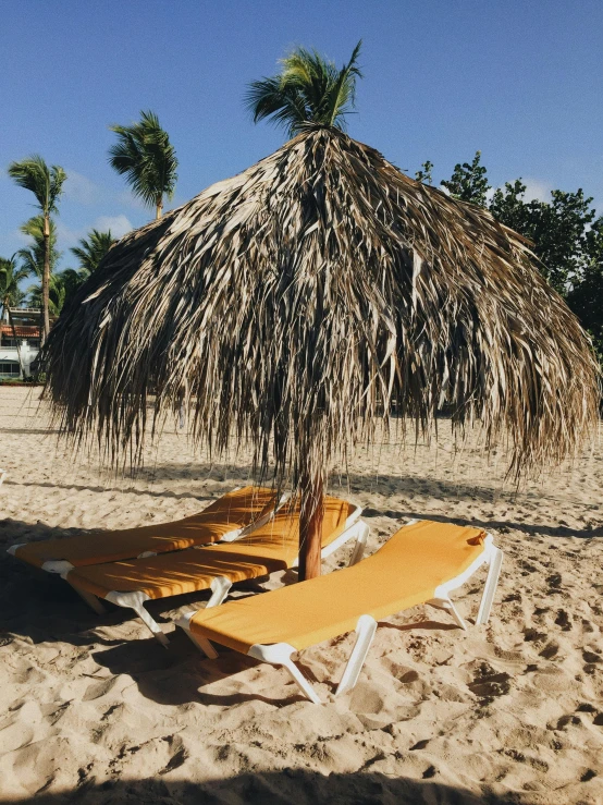 two lounge chairs under a thatched umbrella on a beach, a picture, by Robbie Trevino, trending on vsco, thumbnail, yellow carpeted, sports photo