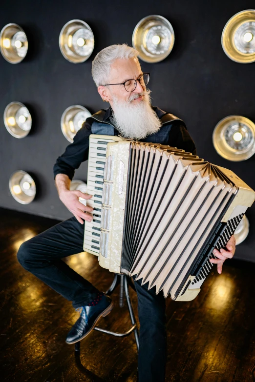 a man sitting on a stool playing an accordion, an album cover, inspired by Mór Adler, reddit, very long silver beard, youtube thumbnail, jean paul gaultier, small in size