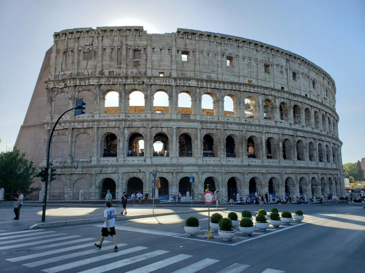 a man is crossing the street in front of the colossion, by Tom Wänerstrand, pexels contest winner, neoclassicism, inside the roman colliseum, avatar image