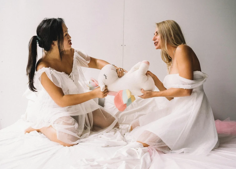 a couple of women sitting on top of a bed, pexels contest winner, white outfit, plush toy, dancing with each other, queer woman