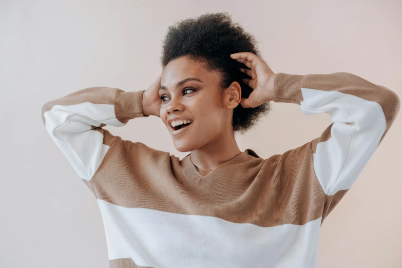 a woman standing with her hands on her head, trending on pexels, brown sweater, happy fashion model, natural hair, gradient brown to white