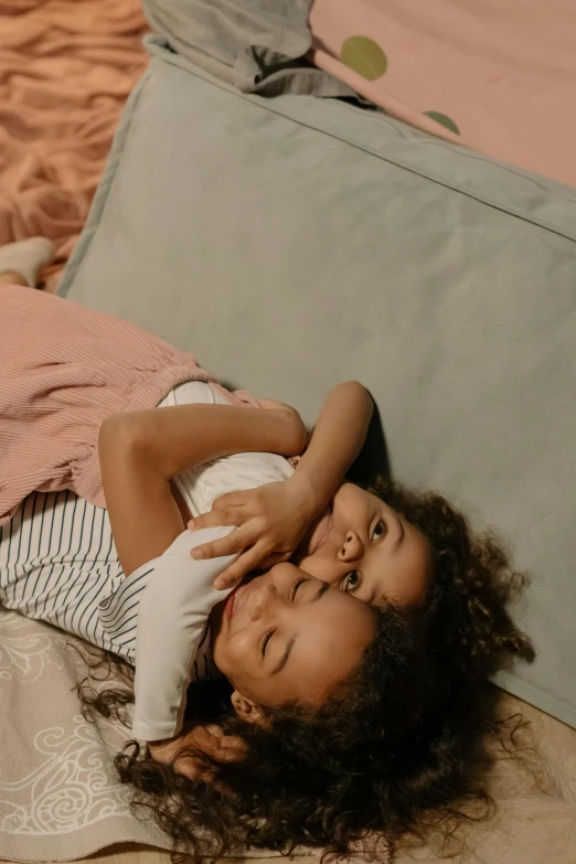 a little girl laying on top of a bed, by Matija Jama, pexels contest winner, incoherents, hugging each other, sisters, softplay, diverse