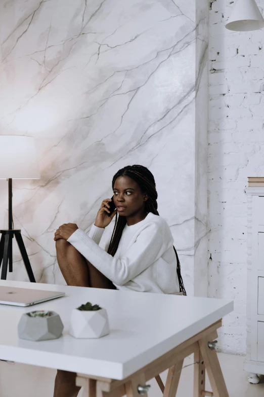 a woman sitting at a table talking on a cell phone, by Chinwe Chukwuogo-Roy, pexels contest winner, minimalism, white marble with gold accents, home office, portrait of tall, marble room