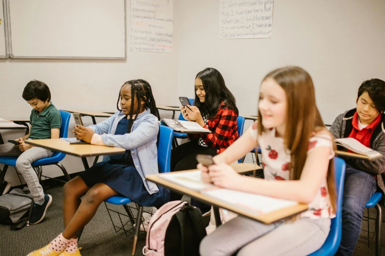 a group of children sitting at desks in a classroom, trending on unsplash, checking her phone, pokimane, full-figure, young girls