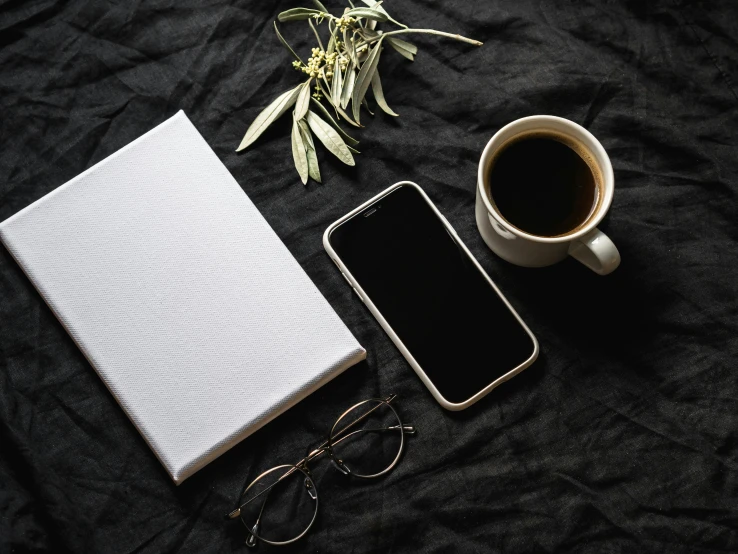 a cell phone sitting next to a book and a cup of coffee, a still life, trending on pexels, minimalism, black square glasses, white and black clothing, black jewellery, white