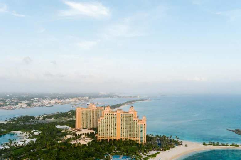 an aerial view of a resort in the middle of the ocean, atlantis in the background, pink marble building, full body image, views to the ocean