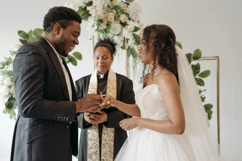 a man putting a wedding ring on a woman's finger, a photo, by Carey Morris, pexels, renaissance, standing in front of the altar, varying ethnicities, in front of white back drop, looking happy