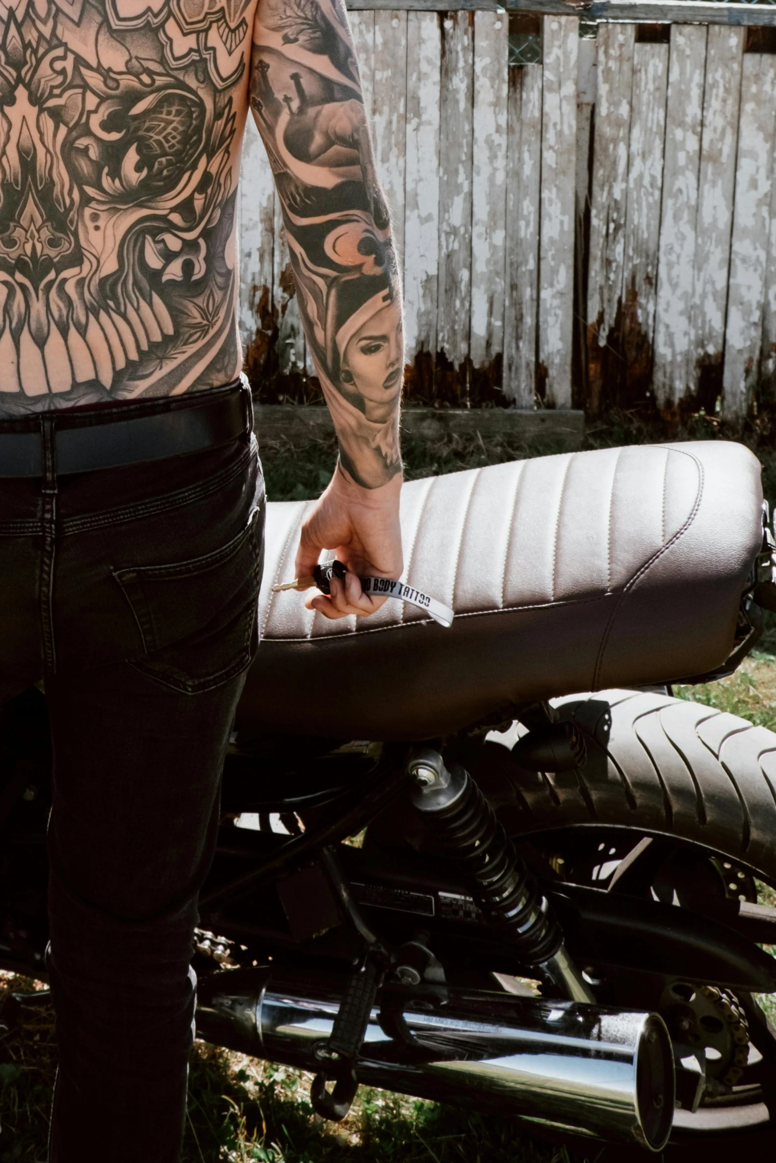 a man with tattoos standing next to a motorcycle, a tattoo, trending on unsplash, holding a small vape, leather padding, matte white paint, close-up shot taken from behind