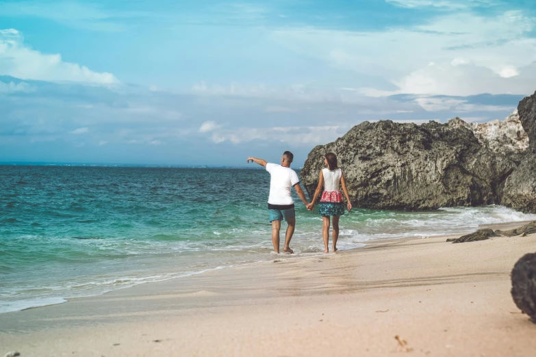 a couple of people standing on top of a sandy beach, on the ocean