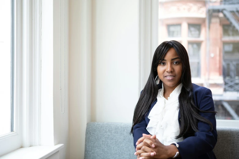 a woman sitting on a couch next to a window, a portrait, by Nina Hamnett, unsplash, hurufiyya, wearing business suit, on a white table, alexis franklin, official photo