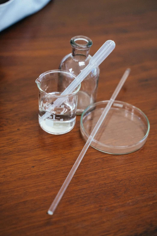 a couple of glasses sitting on top of a wooden table, holding a syringe, product image, botanical, clear