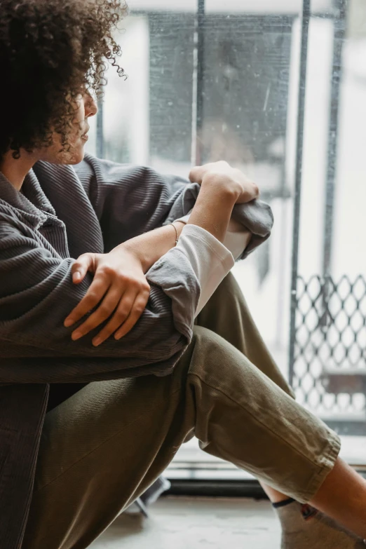 a woman sitting on the floor in front of a window, trending on pexels, wearing a worn out brown suit, she is wearing a wet coat, comforting, non-binary