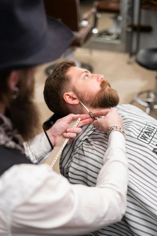 a man cutting another man's hair in a barber shop, long brown beard, wearing collar, curated collections, adam varga