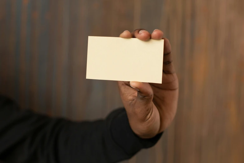 a man holding a blank business card in his hand, by David Simpson, unsplash, slight yellow hue, african american, parchment paper, handcrafted