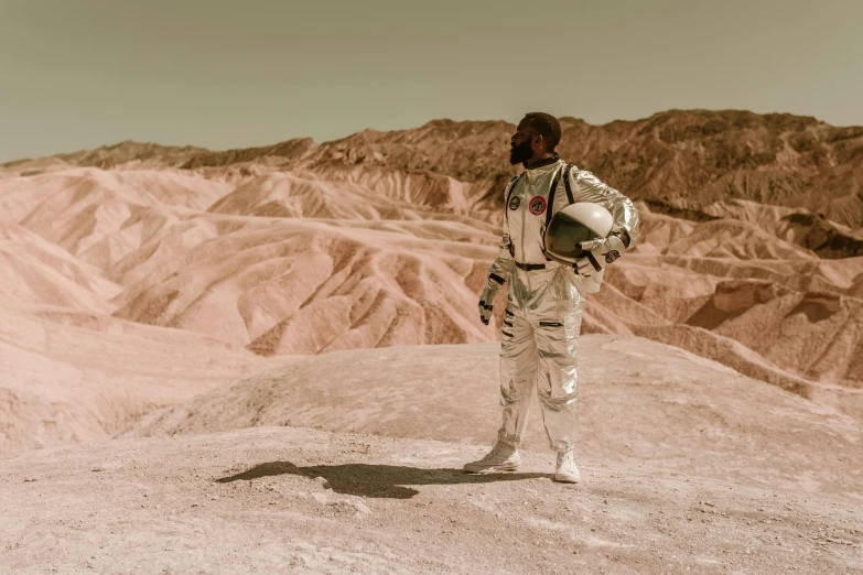 a man in a space suit standing on top of a mountain, pexels contest winner, afrofuturism, brown, movie filmstill, musk ( 2 0 2 4 ), lunar themed attire