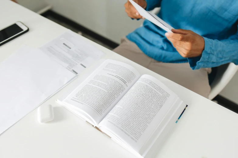 a woman sitting at a table reading a book, white paper, rounded corners, extremely precise, easy to use