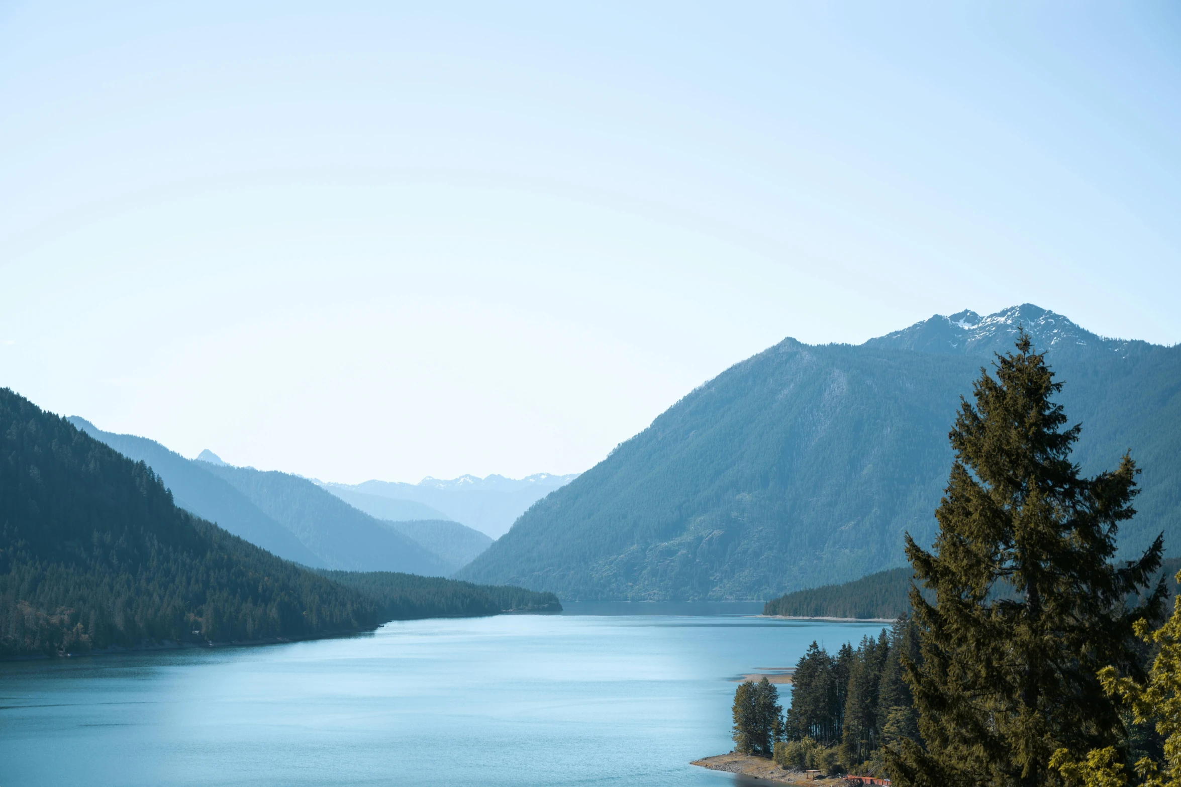 a large body of water surrounded by trees, by Sophie Pemberton, pexels contest winner, with mountains in background, lake blue, album cover, washington