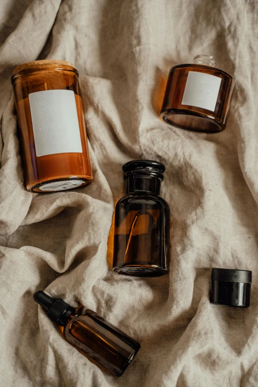 a couple of bottles sitting on top of a bed, a still life, trending on pexels, renaissance, brown robes, skincare, caramel, dreamscape in a jar
