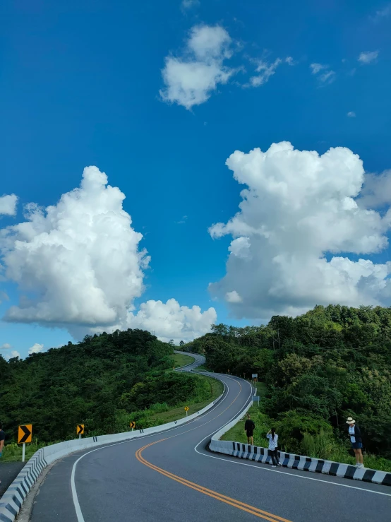 a man riding a motorcycle down a curvy road, by Robbie Trevino, unsplash, process art, big puffy clouds, taiwan, photo on iphone, light blue sky with clouds