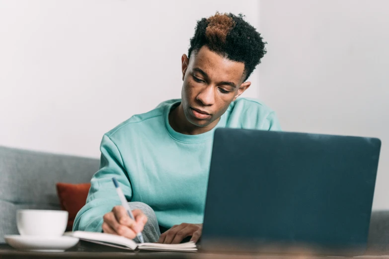 a man sitting at a table working on a laptop, trending on pexels, academic art, with teal clothes, black teenage boy, thumbnail, writing in journal