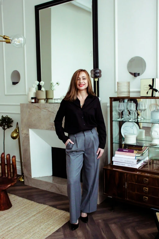 a woman standing in a living room next to a fireplace, a portrait, inspired by Marc-Aurèle de Foy Suzor-Coté, instagram, wearing business casual dress, on a table, miranda otto, studio photo