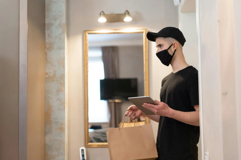 a man wearing a face mask while looking at a tablet, by Julia Pishtar, delivering mail, round mirror on the wall, getting groceries, he is wearing a black t-shirt