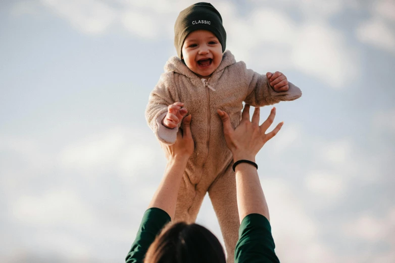 a woman holding a baby up in the air, pexels contest winner, beanie, avatar image, super high resolution, climber