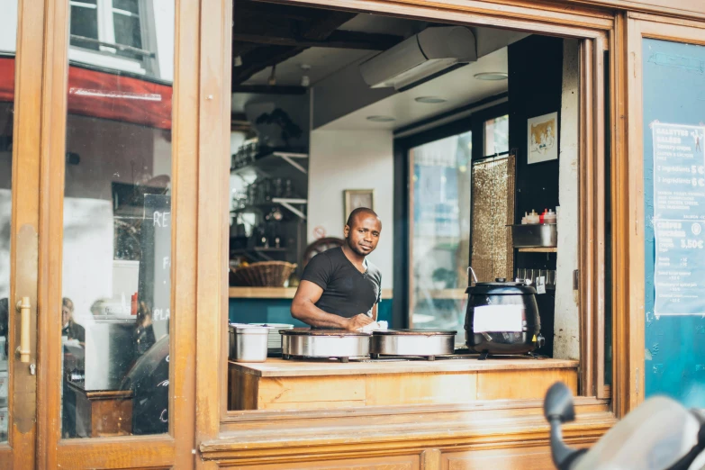 a man standing behind a counter in a restaurant, pexels contest winner, les nabis, pots and pans, orisha, seen from outside, in paris