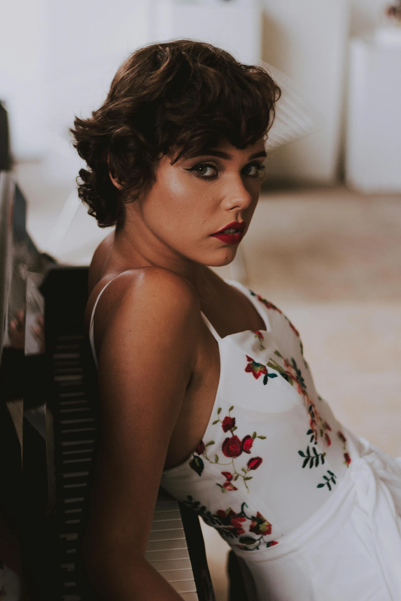 a woman sitting on a chair next to a piano, inspired by Elsa Bleda, pexels contest winner, curly pixie cut hair, isabela moner, eighties-pinup style, profile image