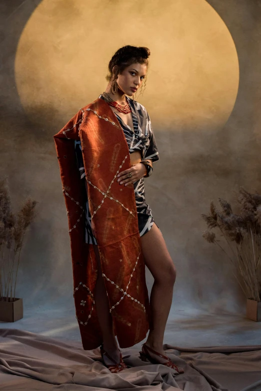 a woman standing in front of a full moon, a portrait, trending on pexels, renaissance, sarong, at a fashion shoot, orange robe, cloth and metal