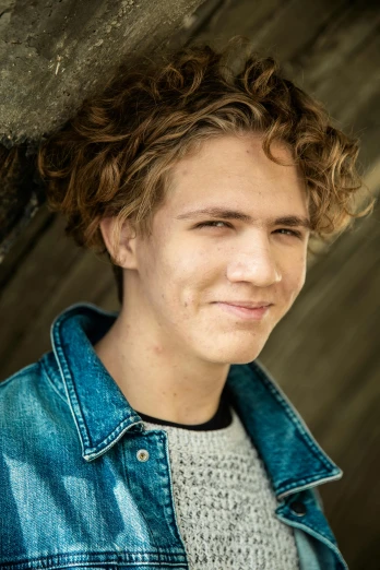 a close up of a person wearing a denim jacket, by Jacob Toorenvliet, light brown messy hair, male teenager, promo image, very slightly smiling