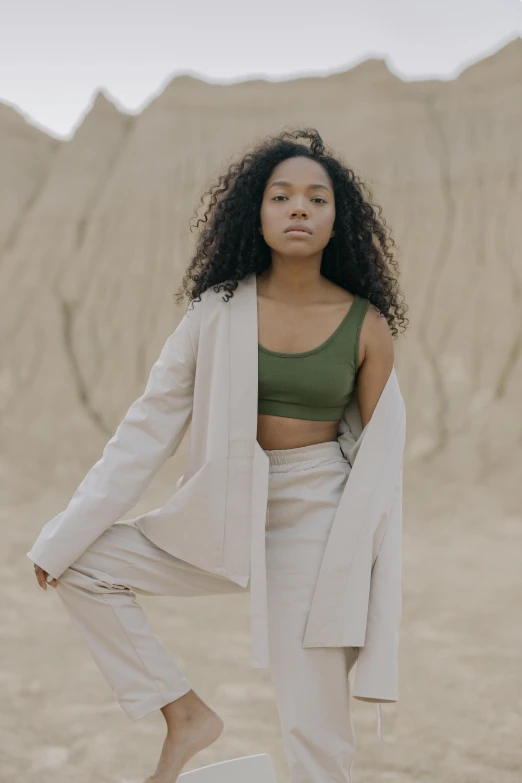 a woman standing on a stool in the desert, an album cover, by Attila Meszlenyi, trending on unsplash, renaissance, wearing a track suit, tessa thompson, wearing green jacket, bare midriff