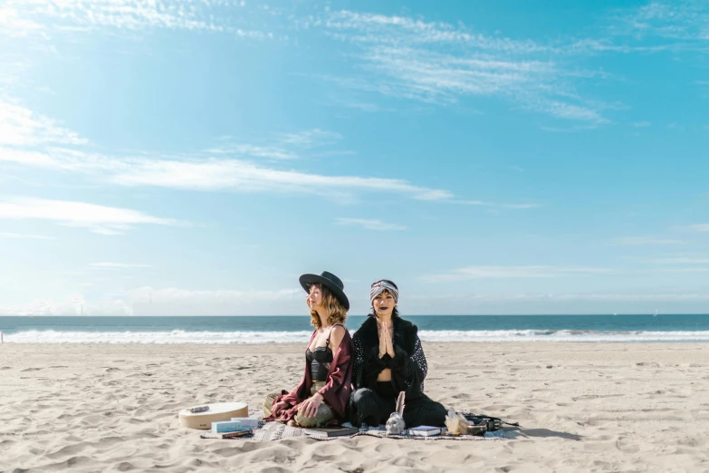 a couple of women sitting on top of a sandy beach, by Julia Pishtar, pexels contest winner, having a picnic, an oversized beret, santa monica beach, australian beach