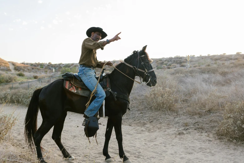a man riding on the back of a black horse, an album cover, unsplash, still from the show breaking bad, black man, hollister ranch, with pointing finger