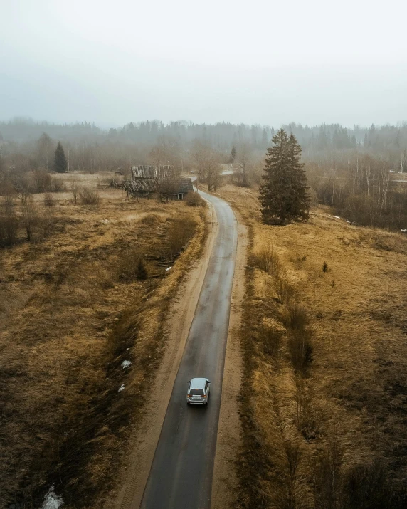 a car driving down a country road on a foggy day, by Adam Marczyński, pexels contest winner, realism, bird\'s eye view, background image, old photo of a creepy landscape, park in background