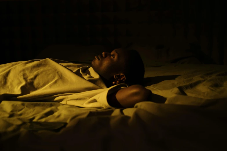 a person laying on a bed in the dark, pexels, hurufiyya, black teenage boy, bathed in light, concerned, african woman