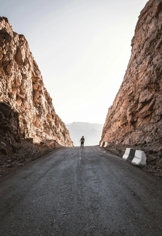 a person standing on the side of a mountain road, by Youssef Howayek, les nabis, canvas, rugged, single street, caramel. rugged