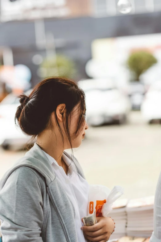 a couple of women standing next to each other, by Reuben Tam, trending on unsplash, set in tokyo bank parking lot, people outside eating meals, with dark hair tied up in a bun, close - up profile