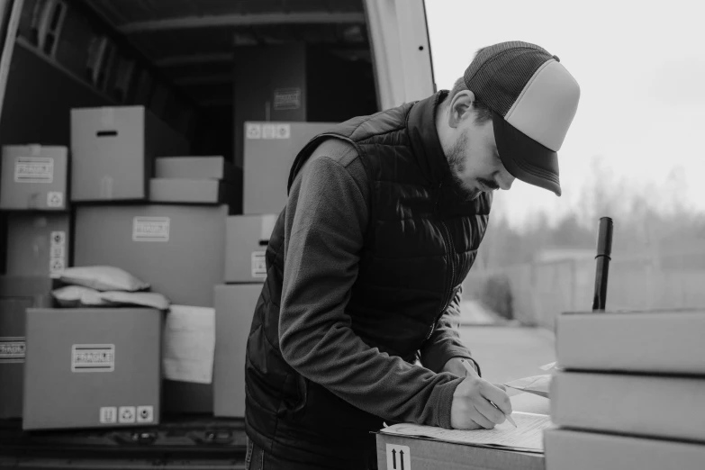 a black and white photo of a man loading boxes, by Kristian Zahrtmann, pexels contest winner, signing a bill, looking to the side, handwritten, jakub rebelka