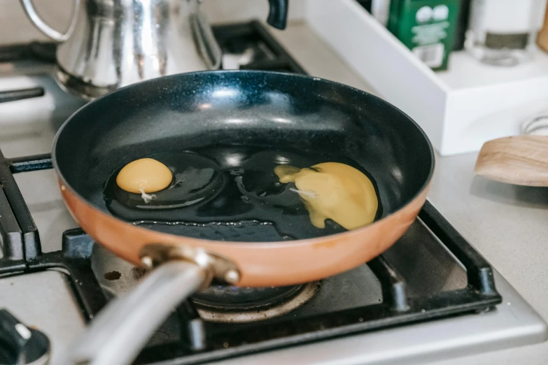 two eggs frying in a frying pan on a stove, by Julia Pishtar, trending on unsplash, liquid golden and black fluid, on kitchen table, thumbnail, caramel